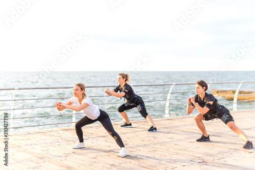 Group of women doing exercises on seashore at sunrise