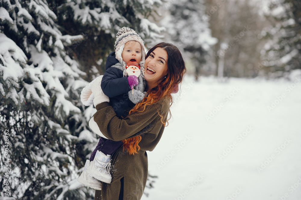 Family have fun in a winter park. Stylish mother in a green sweater. Little girl in a winter clothes. Family have fun in a winter park. Stylish mother in a green sweater. Little girl in a winter clothes.
