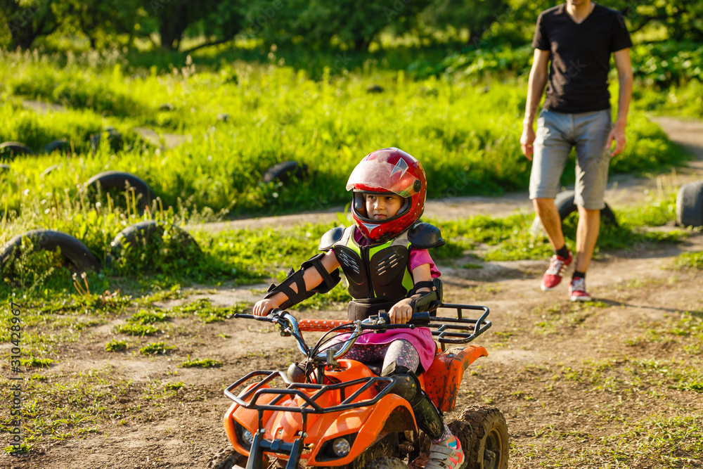 Father and daughter playing on the road at the day time. They driving on quad bike in the park. People having fun on the nature. Concept of friendly family.