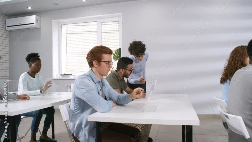 Tracking shot of Caucasian female teacher walking around classroom towards desk, giving instructions for practice to students, performing tasks on interactive touchscreen devices. Template for AR, VR. Tracking shot of Caucasian female teacher walking around classroom towards desk, giving instructions for practice to students, performing tasks on interactive touchscreen devices. Template for AR, VR.