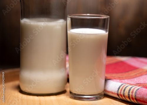 Bottle of milk, a glass and a checkered napkin. Rustic milk on a wooden background. Still life with rustic milk.