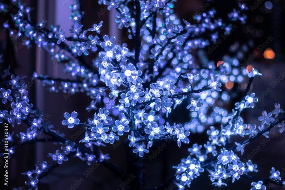 Luminous garland of decorative flowers on a tree. Christmas tree decorated with bright bulbs Luminous garland of decorative flowers on a tree. Christmas tree decorated with bright bulbs