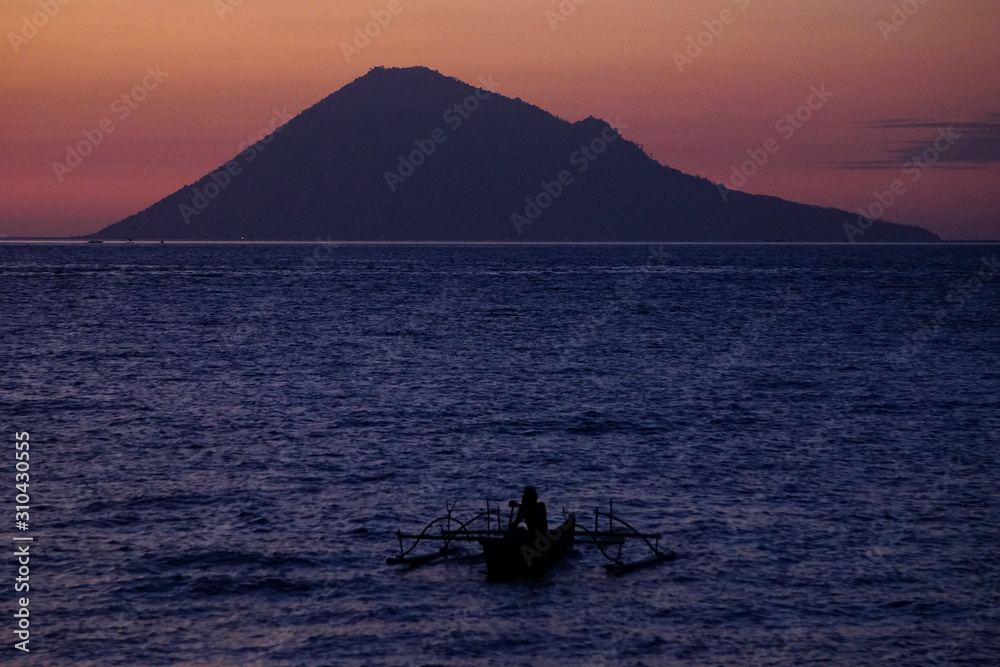 Manado, Indonesia, July 29, 2017. Fisherman sail alone when dusk with the background of Manado Tua Island. Manado, Indonesia, July 29, 2017. Fisherman sail alone when dusk with the background of Manado Tua Island.