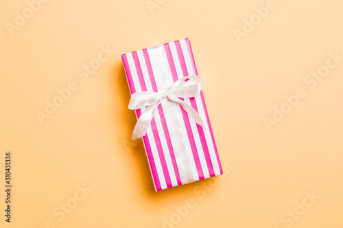 wrapped Christmas or other holiday handmade present in paper with white ribbon on orange background. Present box, decoration of gift on colored table, top view with copy space © sosiukin