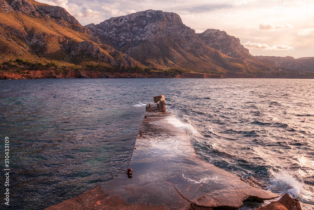 Stone jetty/pier El Calo near Betlem and Colonia De Sant Pere, green hills  with beautiful light, afternoon with blue sky and white clouds, Mallorca,  Spain. Stock Photo | Adobe Stock