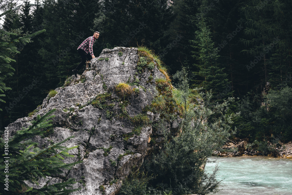 Man on a large stone, a boulder, among the incredibly beautiful river of turquoise color, Dolomites mountains, Camping Olympia Fiames, Cortina Ampezzo Italy.