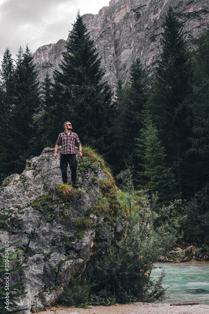 Man on a large stone, a boulder, among the incredibly beautiful river of turquoise color, vertical photo. Dolomites mountains, Camping Olympia Fiames, Cortina Ampezzo Italy. Man on a large stone, a boulder, among the incredibly beautiful river of turquoise color, vertical photo. Dolomites mountains, Camping Olympia Fiames, Cortina Ampezzo Italy.
