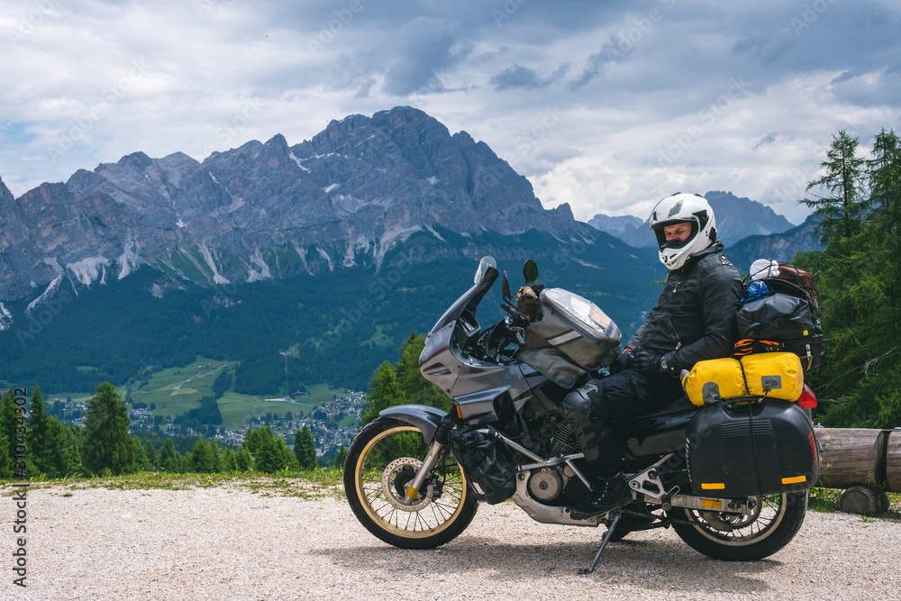 Biker man is sitting on adventure touring motorcycle take a rest after long road trip, Top mountains on background, tourism travel concept, copy space. Dirt road, freedom