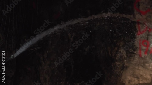 Person wearing ppe hosing a down rock face with water in an underground gold mine photo