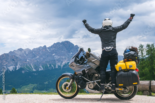 Concept of destination. conquering the top, two hands up, biker man with touring motorcycle on dirt road, 