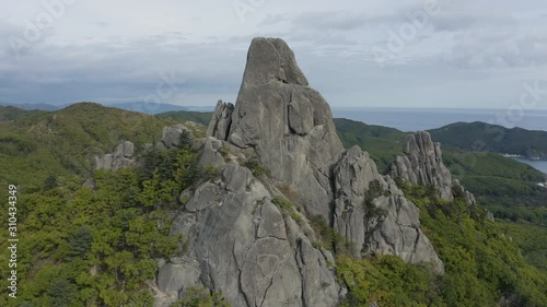 Aerial view of a mountain ridge with an ancient megalithic stones formations on top of the forested mountains and reveal of ocean coastline in far distance. photo