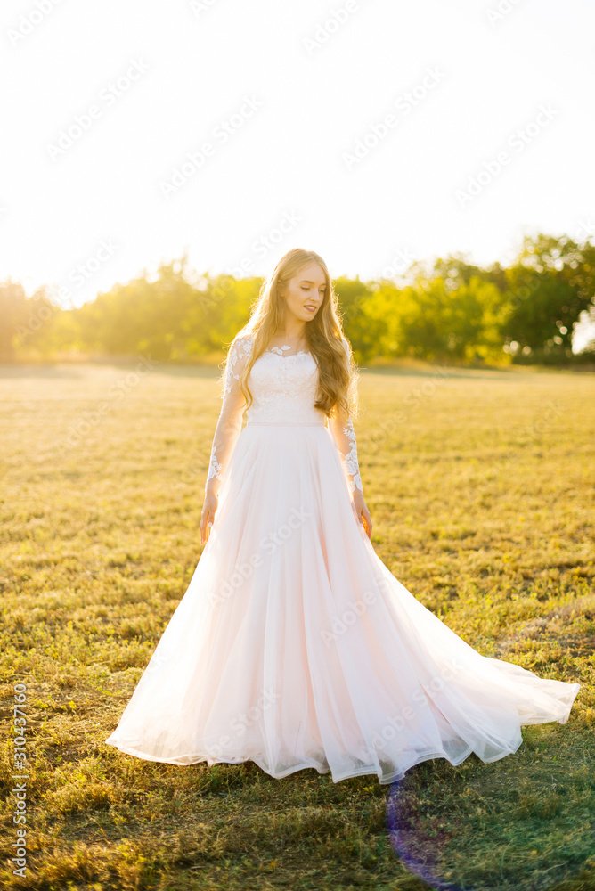 Young woman is dressed in a bridal dress and looking away in the field.