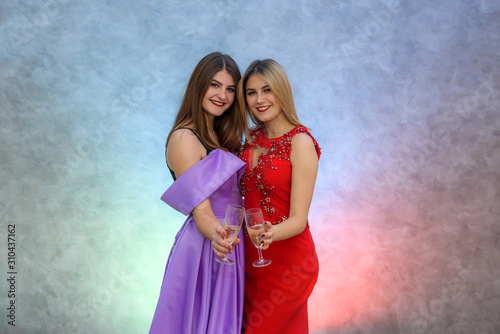 Blonde and brunette woman in elegant evening dresses posing with champagne glasses