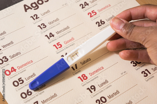 Woman holding a positive pregnancy test on a wooden desk