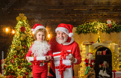 Family holidays and childhood concept. Little child with Santa Claus and Christmas gift at home. Santa Claus and child with Christmas present. Kid boy and father in Santa costume and beard. Christmas.