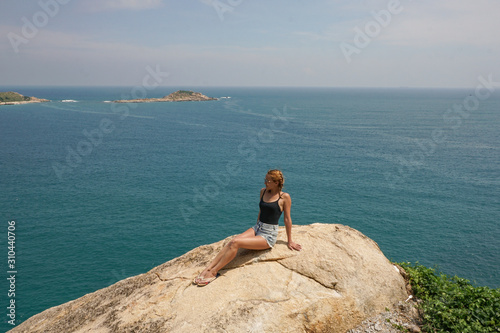The girl on the rock with view on the ocean with beach and mountains