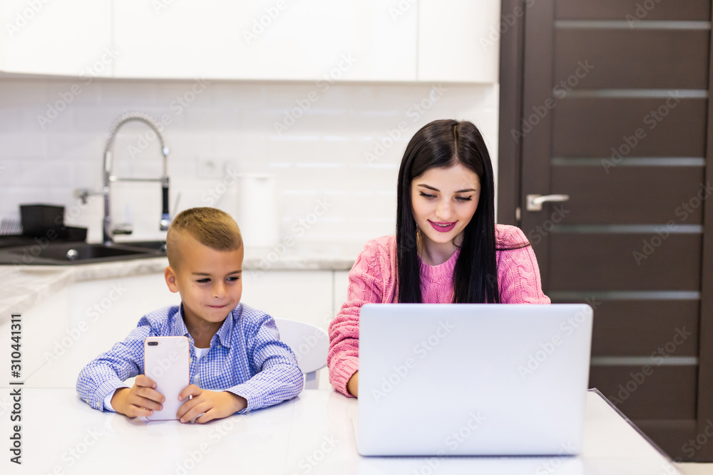 Young Mother working on laptop at home, while her child is bored back play on phone Young Mother working on laptop at home, while her child is bored back play on phone