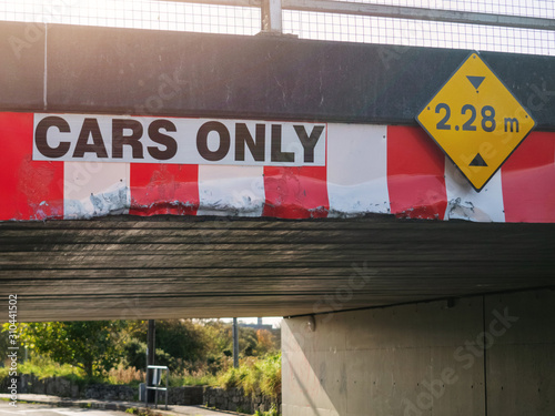Low bridge with visual damage by careless drivers. Yellow height warming in meters. white and red vertical warning stripes, Cars only sign. Concept danger at road and lack of attention.