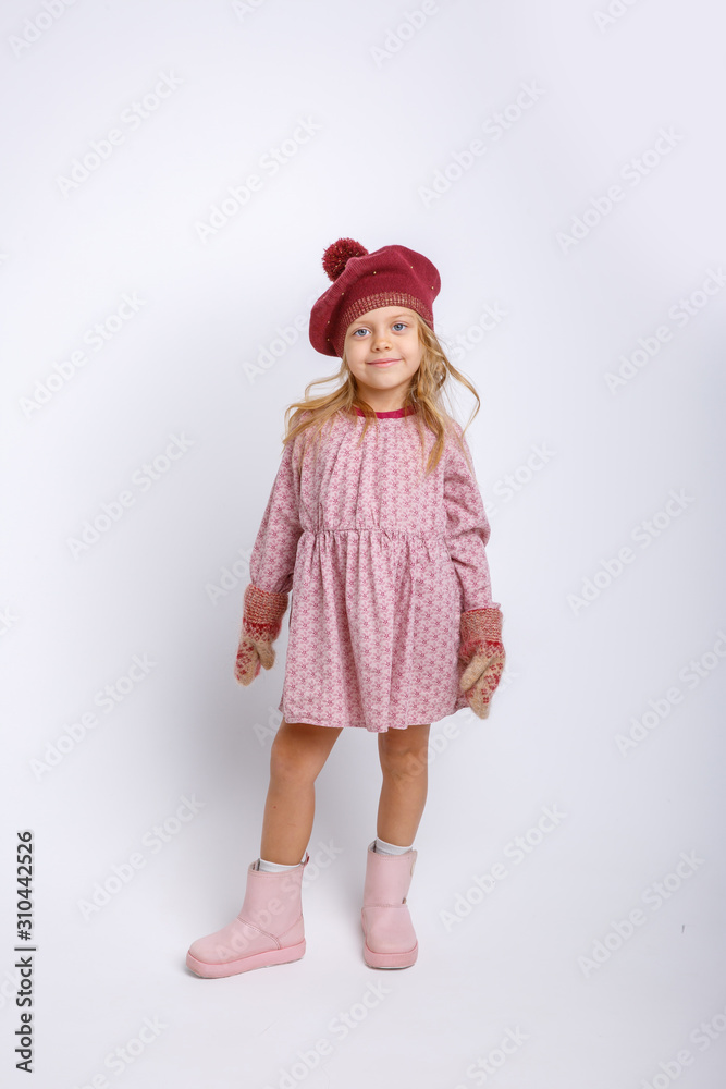 portrait of a small smiling girl in mittens and hat on a gray background