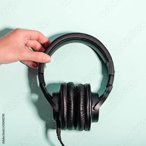 Black massive headphones in female hand on pastel background, copy space. Modern technology flat lay with over-ear earphones in woman hand, modern lifestyle concept