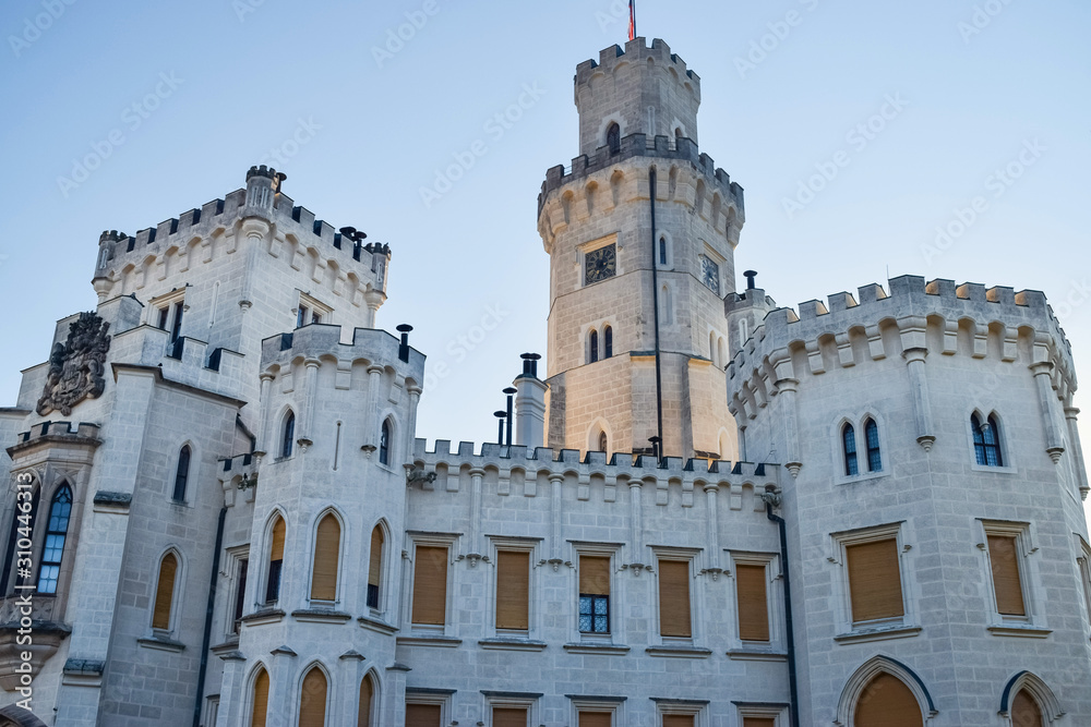 Tower of ancient European castle with clock and windows and battlements on roof for defense