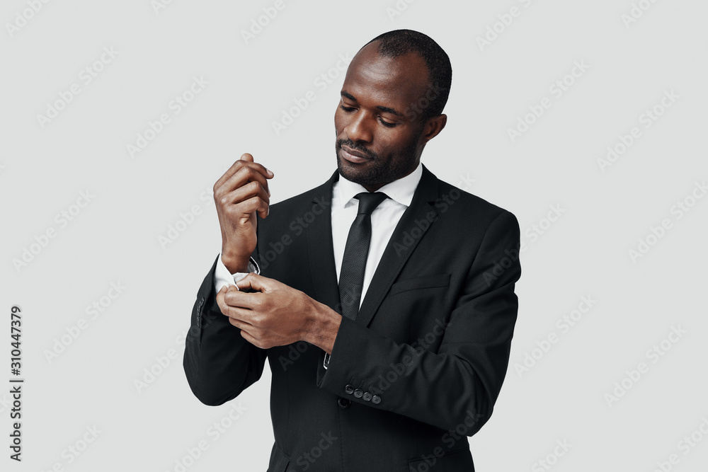 Stylish young African man in formalwear adjusting sleeve while standing against grey background Stylish young African man in formalwear adjusting sleeve while standing against grey background