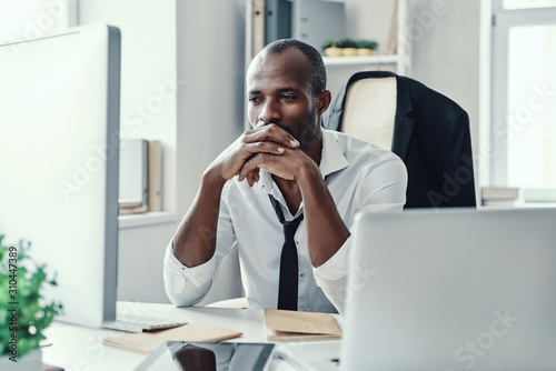 Thoughtful young African man in formalwear looking straight while working in the office