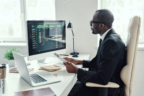 Concentrated young African man in formalwear using modern technologies while working in the office