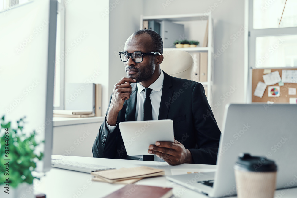Concentrated young African man in formalwear using modern technologies while working in the office Concentrated young African man in formalwear using modern technologies while working in the office