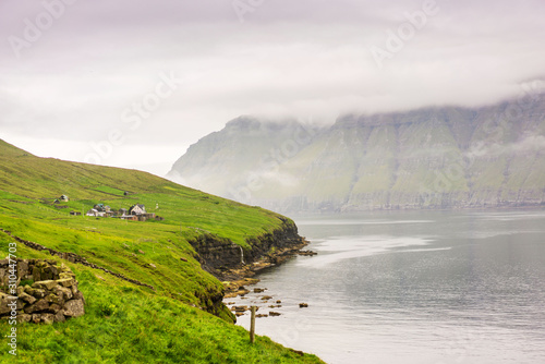 Remote small village located near a fjord, green mountains covered with thick fog. Faroe Islands, Denmark.