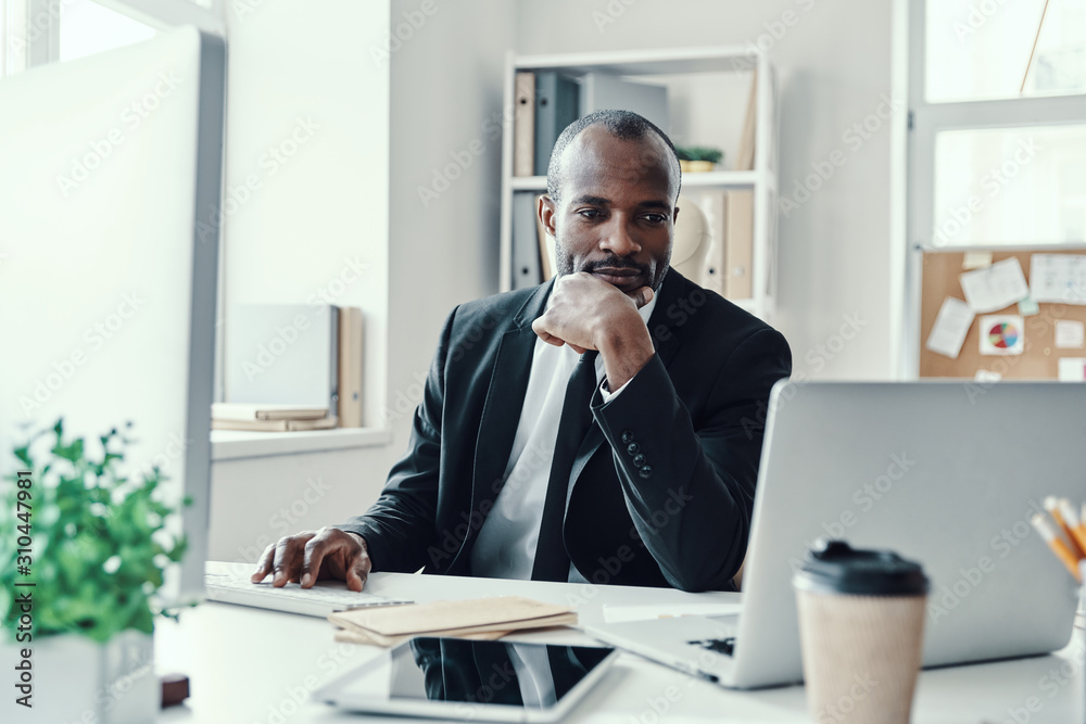 Concentrated young African man in formalwear using modern technologies while working in the office Concentrated young African man in formalwear using modern technologies while working in the office