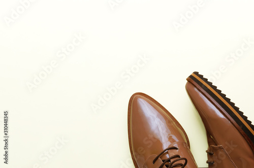 Stylish brown female patent leather shoes on pastel light yellow background. Fashion blog, magazine, beauty concept. Minimal composition. Flat lay, top view. Copy space