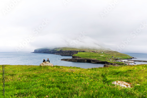 Young couple of traveller observing panorama of Nolsoy island. Green field, sea and overcast sky. photo