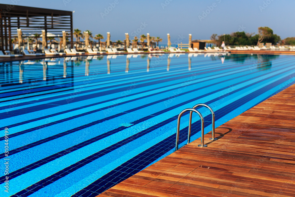 Naklejka premium pool with wooden banks in the morning with palm trees on the beach umbrellas stacked sun beds empty without people