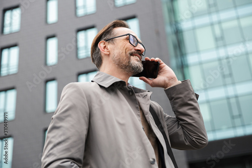 Image of smiling businessman talking on cellphone while standing