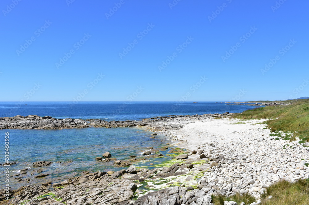 Beach with white rocks, grass and blue sky. Galicia, Spain.