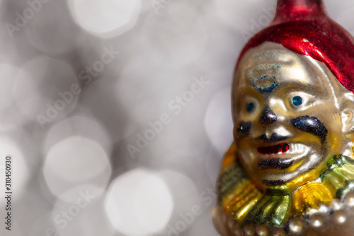 Vintage decorative christmas bauble in a shape of a crown jester against a silver bokeh blury star background.