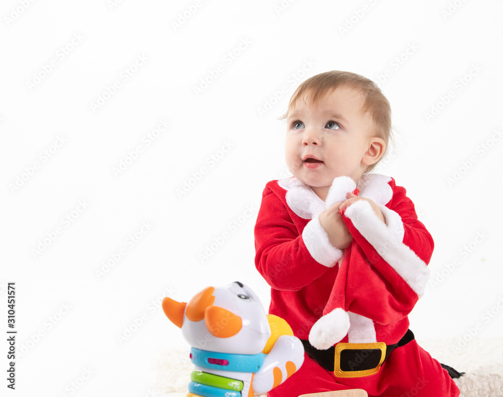 Baby disguised as Santa Claus sitting on the floor while an adult hand grabs his hat from his hands