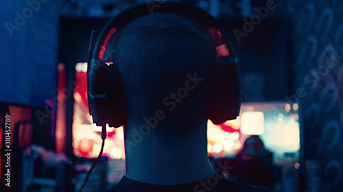 a gamer is sitting in front of a large monitor with headphones, he is an esportsman, a guy of European appearance is shot from the back, a silhouette in headphones against the background of a monitor 