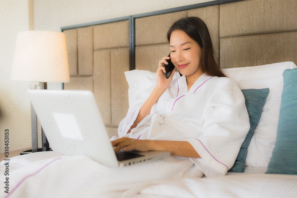 Portrait beautiful young asian women using laptop or computer with mobile smart phone on bed