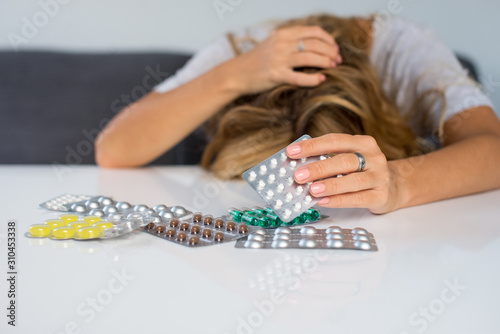 Young depressed woman looking down at pills. Woman sleeping on desk after taking pills. Out of focus woman with some pills from her medical treatment on a table in the foreground