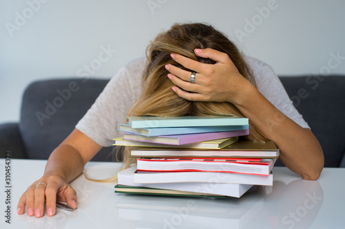 Woman student boring reading book at library with a lot of books in university. A sudent disheartened reading book for examination photo