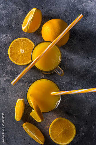  Glass of fresh orange juice, ripe orange fruits and slices on a gray stone background Freshly squeezed orange juice with a straw