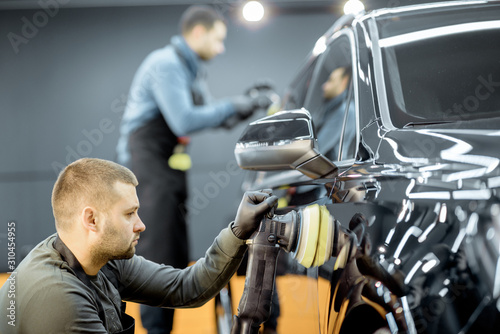 Fotografi Two workers polishing vehicle body with special grinder and wax from scratches at the car service station