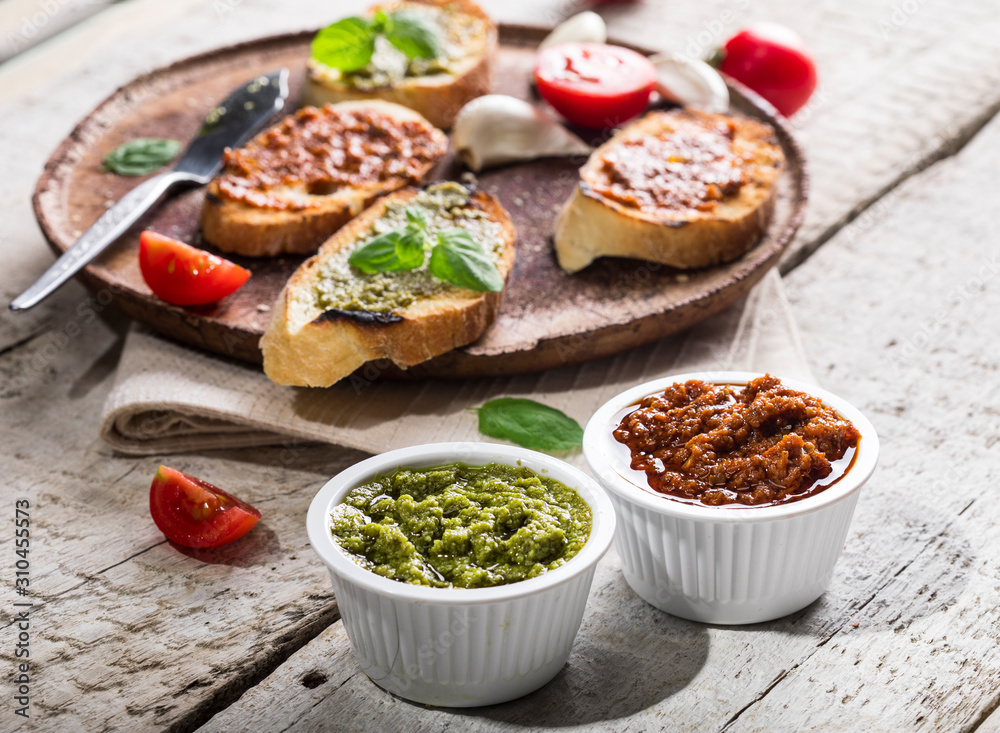 Sliced traditional toast bread with basil and tomato pesto on a cutting board and white table