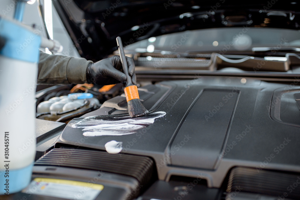 Man performs a professional car cleaning, washing engine with brush and detergent at the service station, close-up view Man performs a professional car cleaning, washing engine with brush and detergent at the service station, close-up view