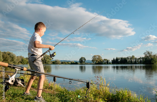 Boy fishing on a lake. Beautiful fish pond in Badin, near Banska Bystrica, Slovakia. Fishing place. Shining sun over the fish pond in summer day. Child holding fishing rod. Little fisherman.
