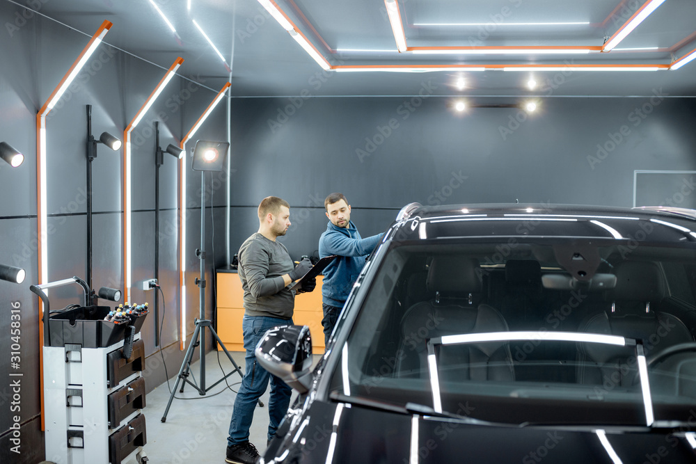 Two car service workers examining vehicle body for scratches and damages while taking a car for professional automotive detailing Two car service workers examining vehicle body for scratches and damages while taking a car for professional automotive detailing