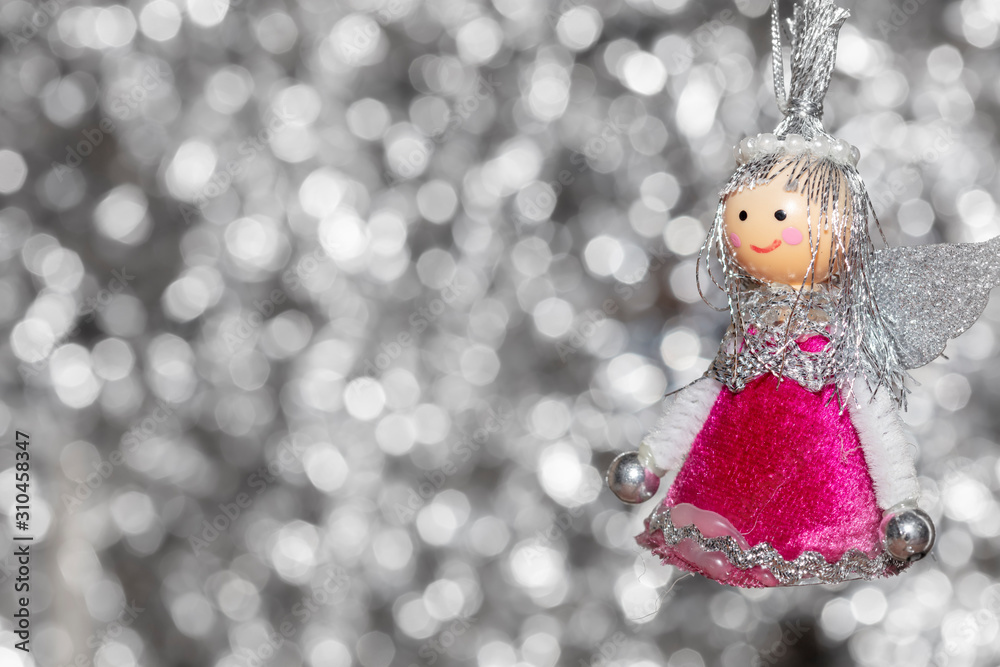 Vintage decorative christmas bauble in a shape of an angel against a silver bokeh blurry star background.