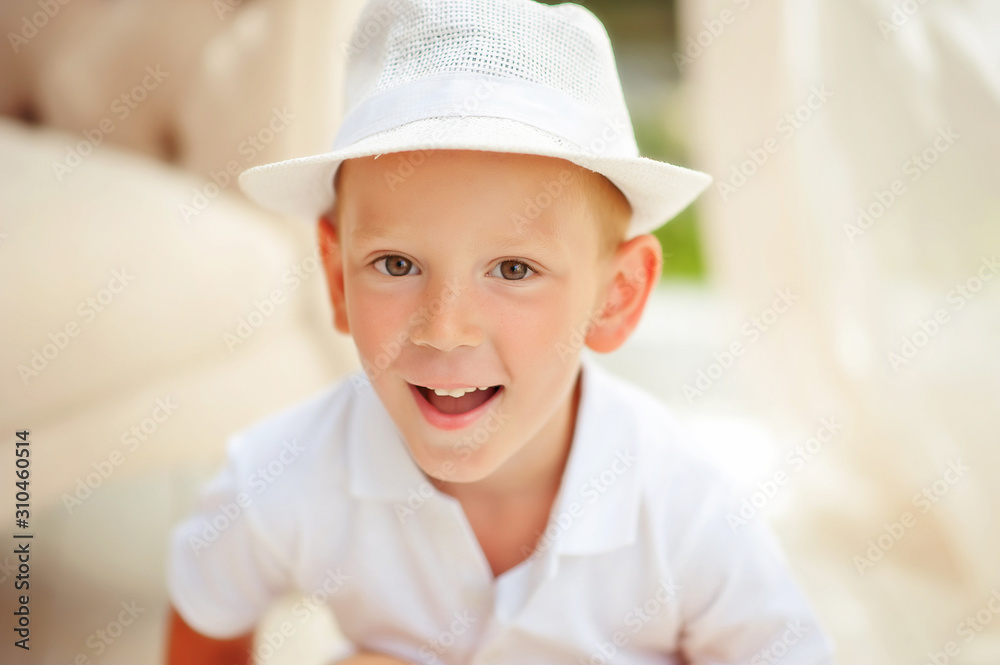 Close up portrait of 5 years old smiling boy in white summer hat and white shirt in summer pavilion. Emotional laughing child. Summer clothes for boys. Happy childhood. Children in summer Close up portrait of 5 years old smiling boy in white summer hat and white shirt in summer pavilion. Emotional laughing child. Summer clothes for boys. Happy childhood. Children in summer